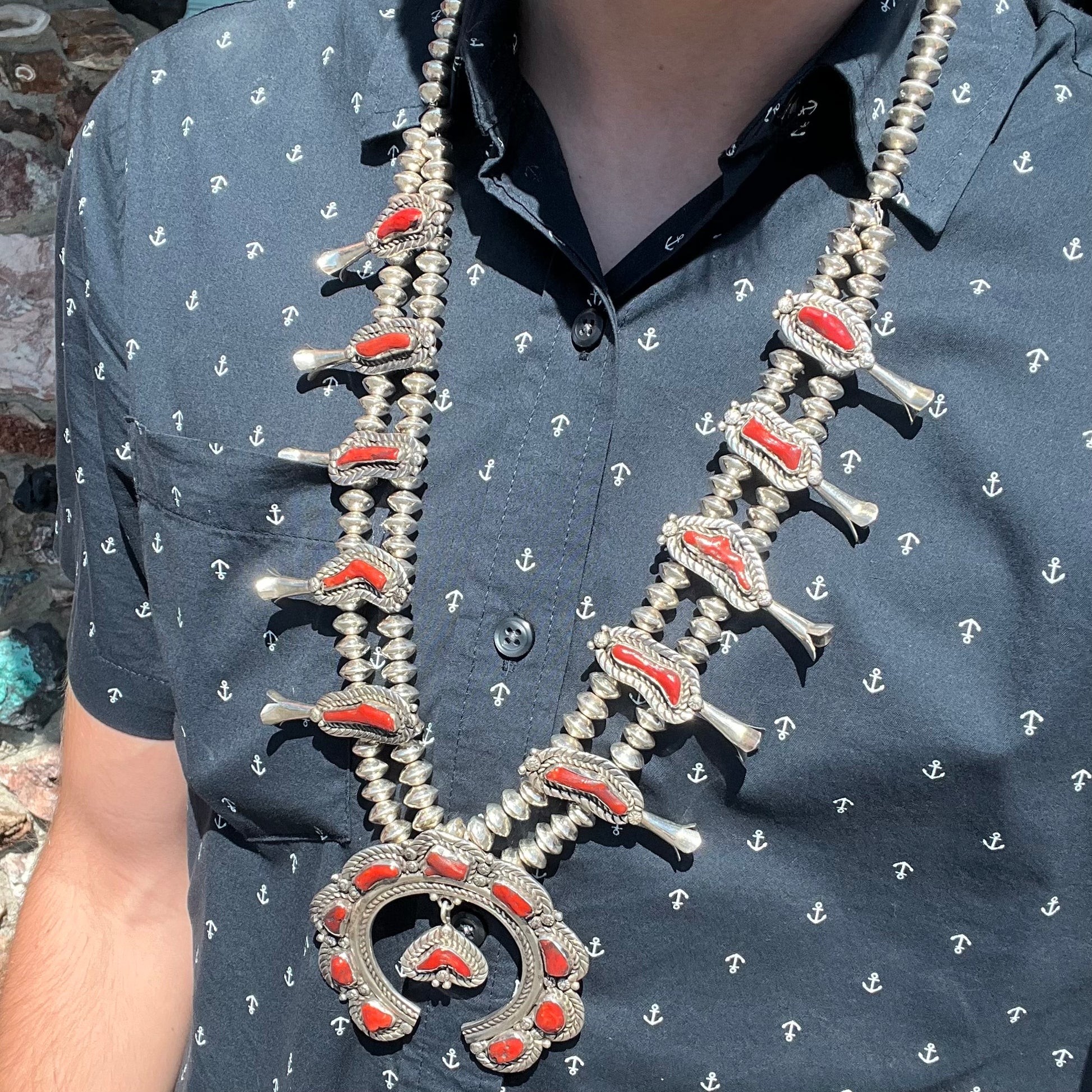 A Navajo style squash blossom necklace set with red coral branches, handmade by artist Delbert Chatter.