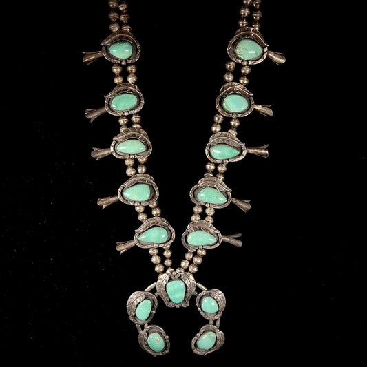 A handmade silver Navajo style squash blossom necklace set with green Kingman turquoise.