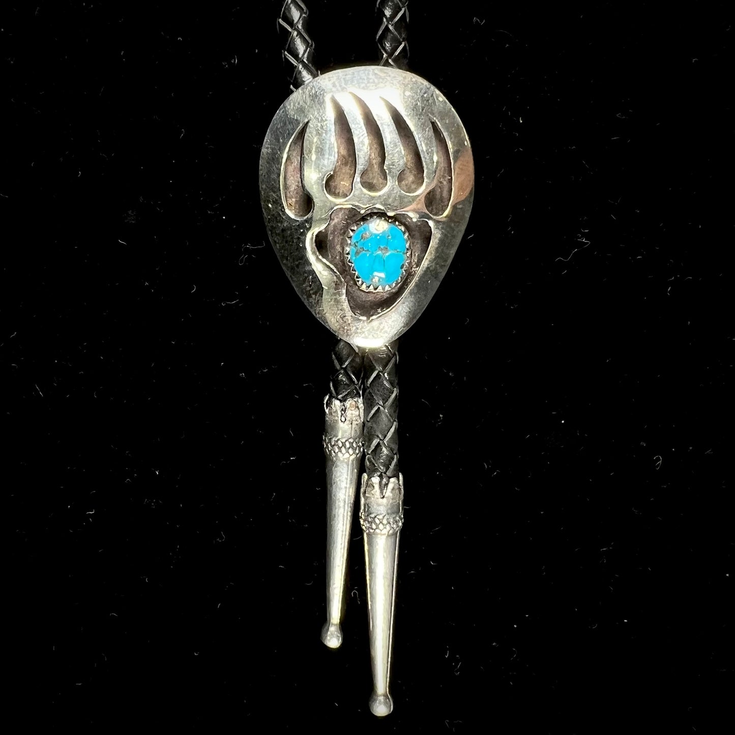 A sterling silver bolo tie in the shape of a bear's paw set with a Morenci turquoise stone.