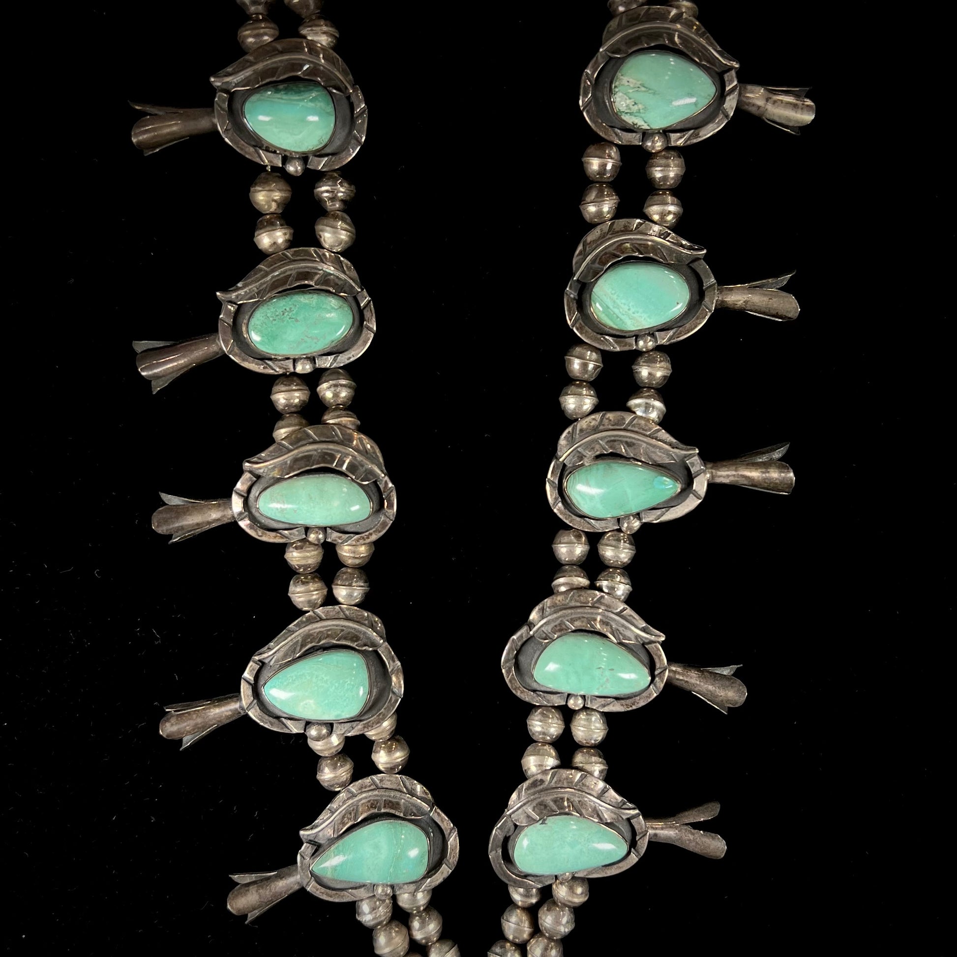 A handmade silver Navajo style squash blossom necklace set with green Kingman turquoise.