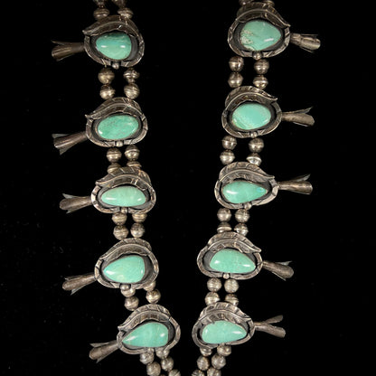 A handmade silver Navajo style squash blossom necklace set with green Kingman turquoise.