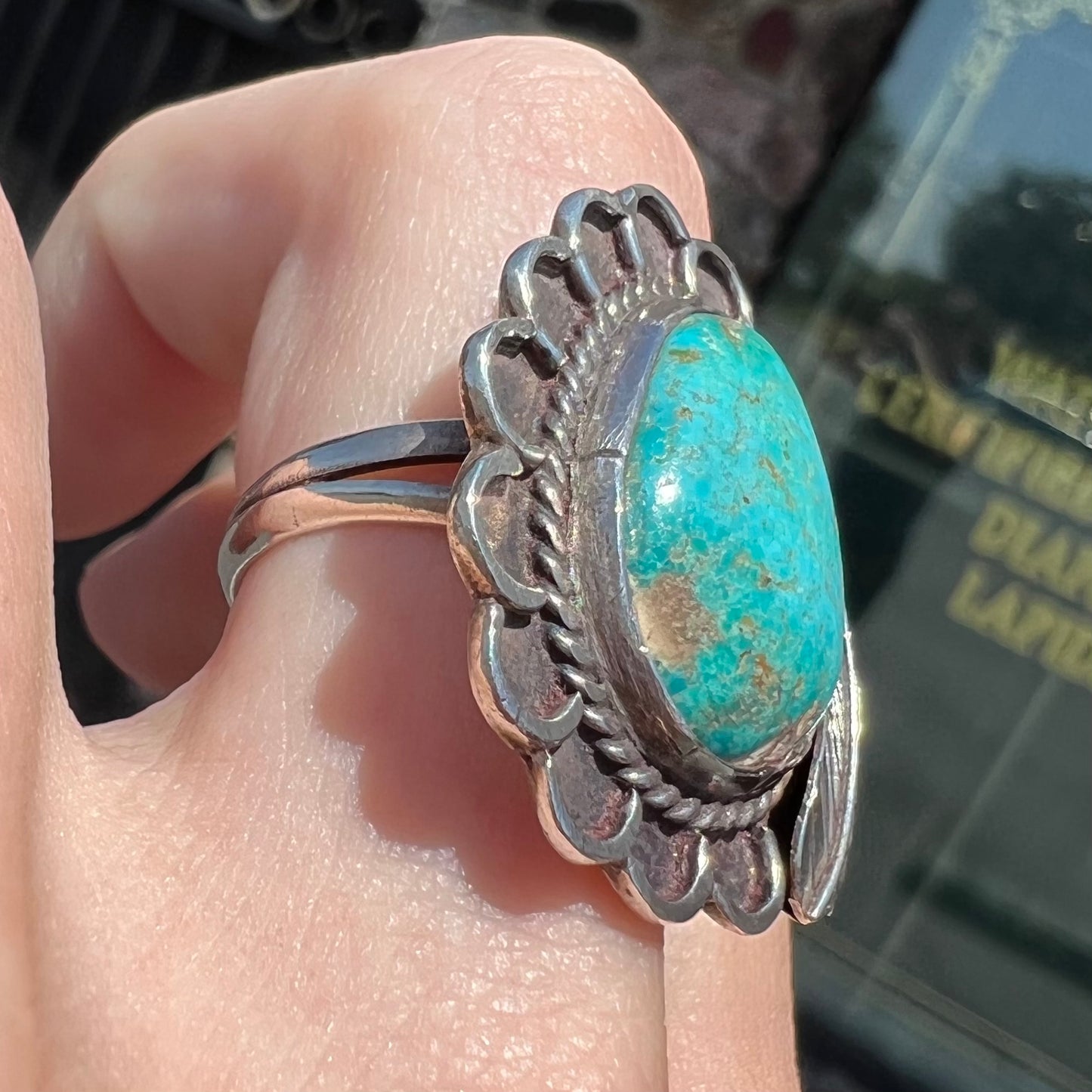 A sterling silver Navajo style ring.  The ring is set with a turquoise stone from Pilot Mountain.  There is a feather decoration next to the stone.