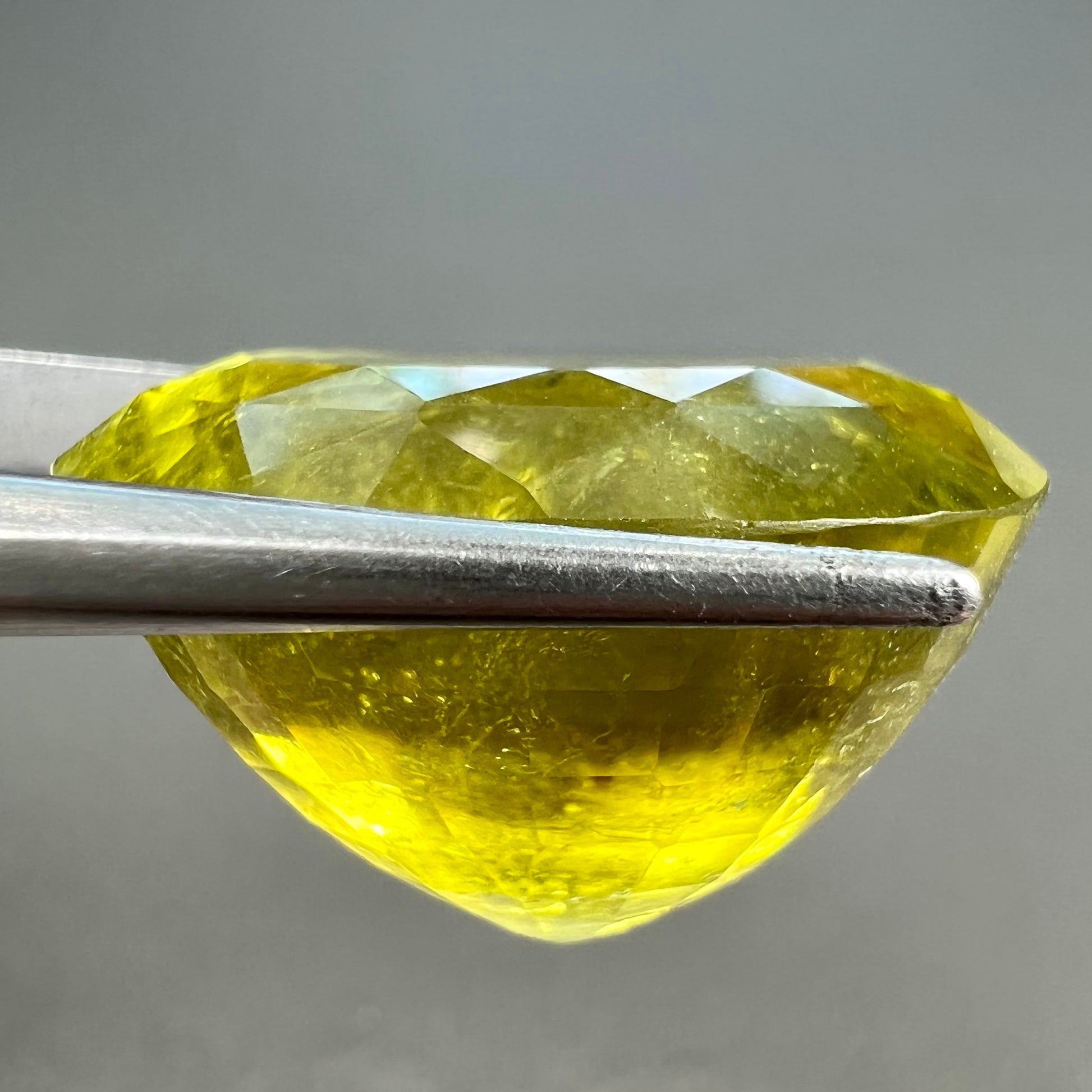 A loose, faceted oval cut green tourmaline stone.  The color is an almost neon yellow-green.