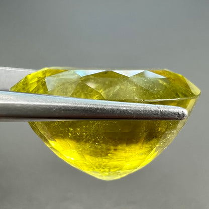 A loose, faceted oval cut green tourmaline stone.  The color is an almost neon yellow-green.