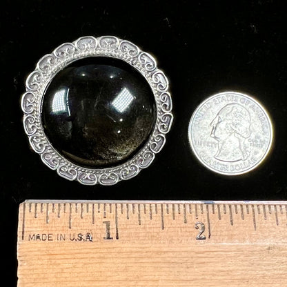 A sterling silver pendant/brooch bezel set with a round cabochon cut black sheen obsidian stone.