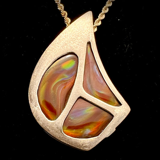A men's gold pendant set with three fire agate stones.  The fire agate resembles an oil slick puddle.