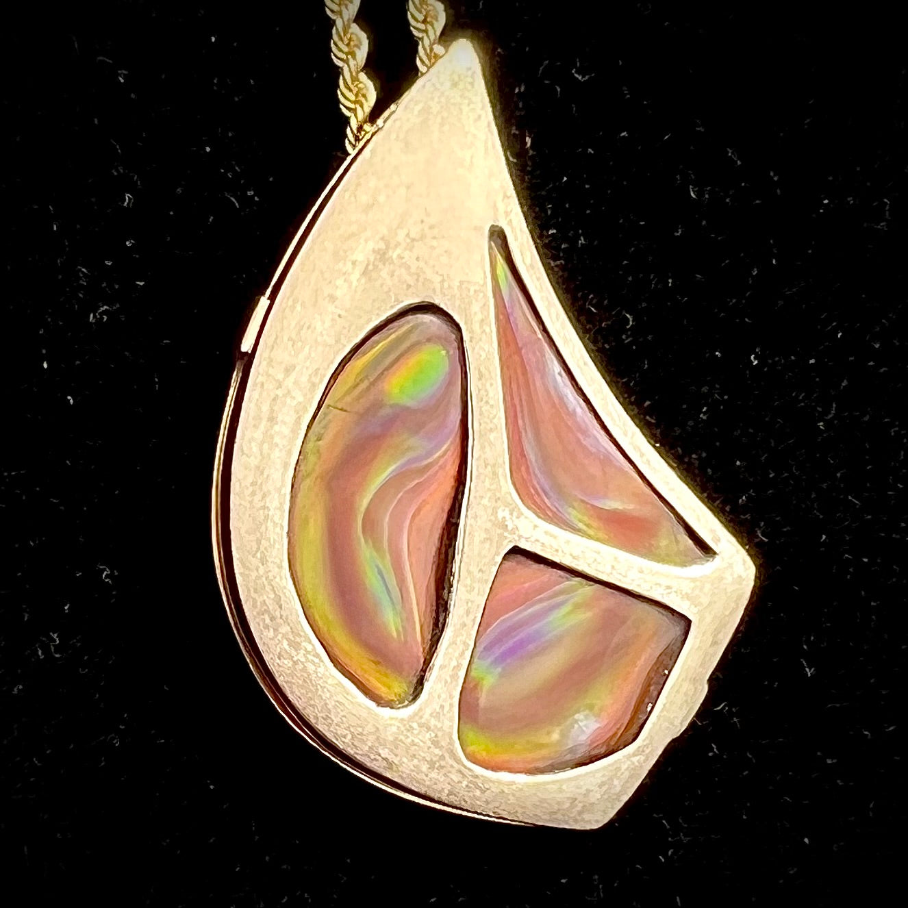 A men's gold pendant set with three fire agate stones.  The fire agate resembles an oil slick puddle.