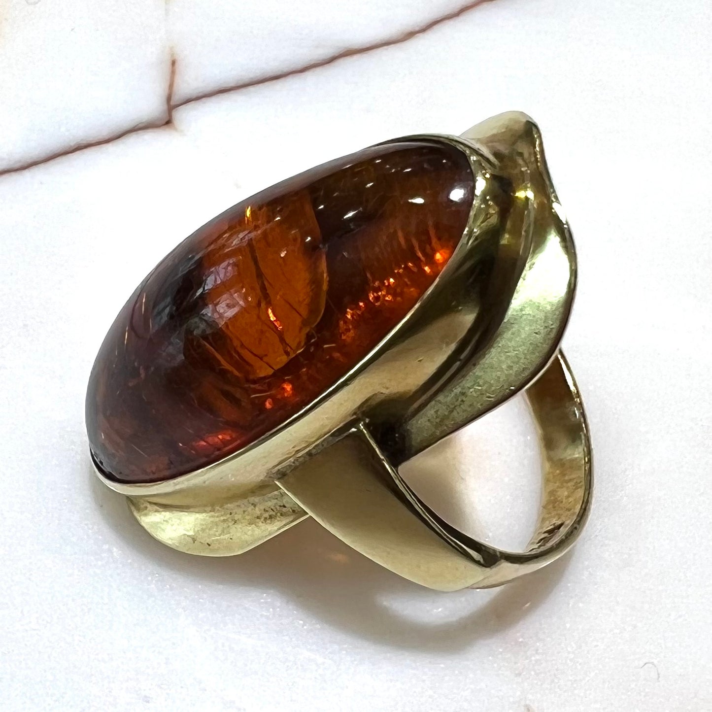 An oval cabochon cut Baltic amber stone set in a yellow gold ring and stamped "AMBER GUILD."