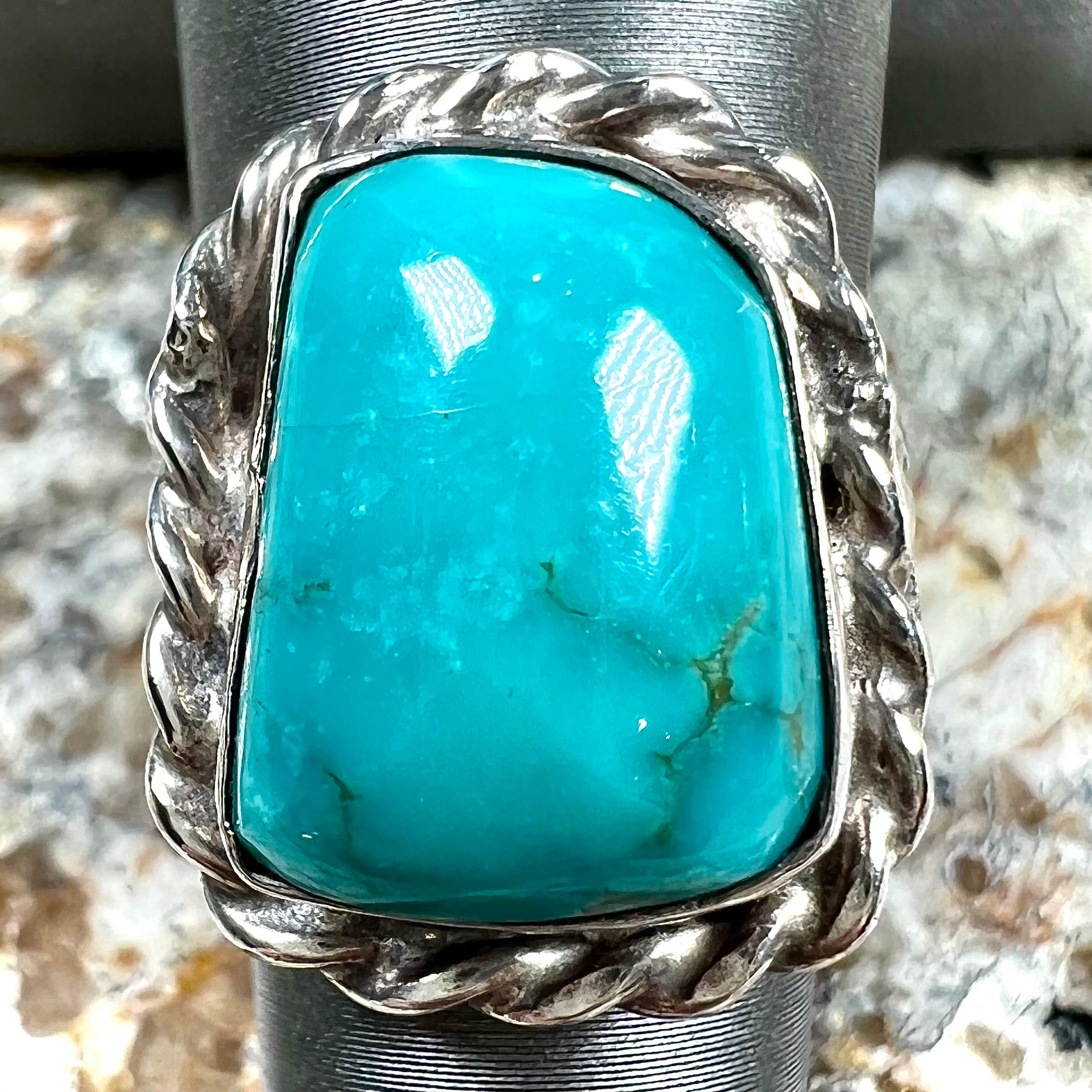 A sterling silver turquoise split shank ring.  There is a handmade silver rope around the turquoise.