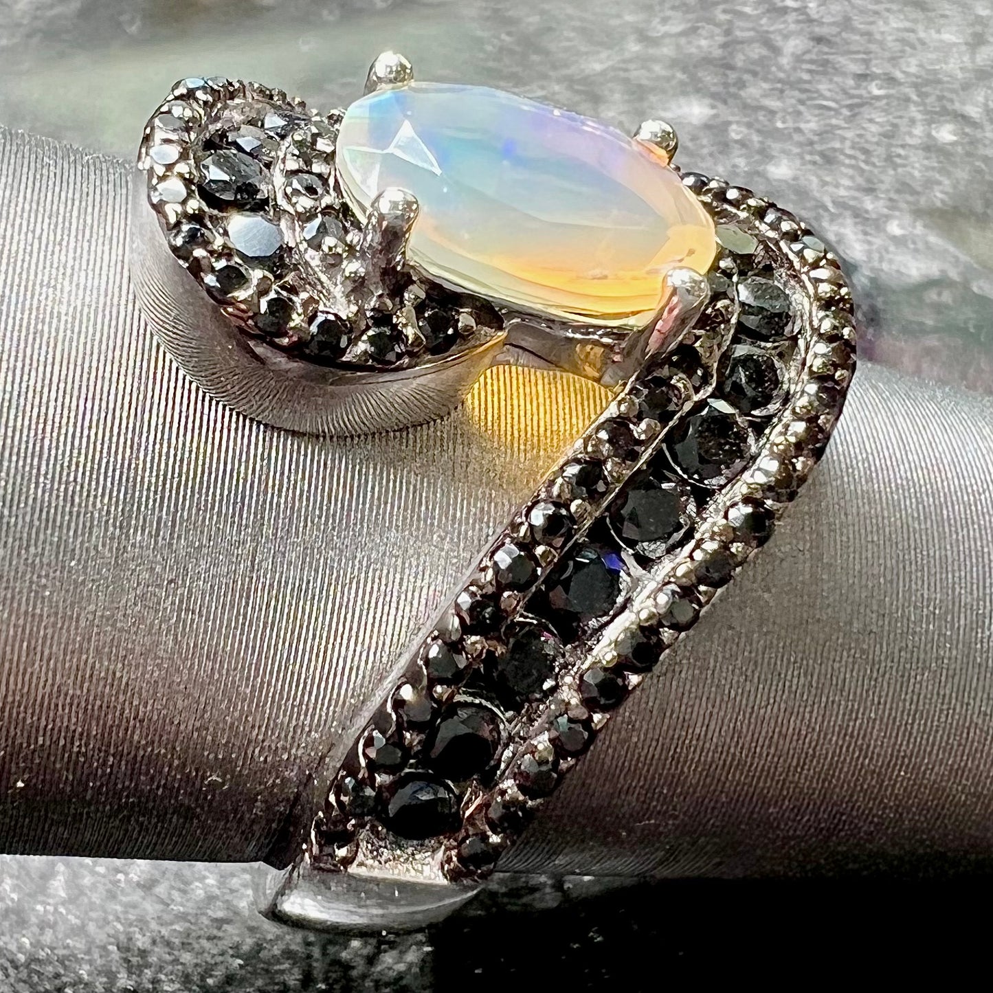 A sterling silver ring set with round black spinel stones and an oval cut, faceted Ethiopian opal.