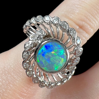 A white gold ring featuring a round cabochon cut black opal set in a swirl of round cut diamonds.