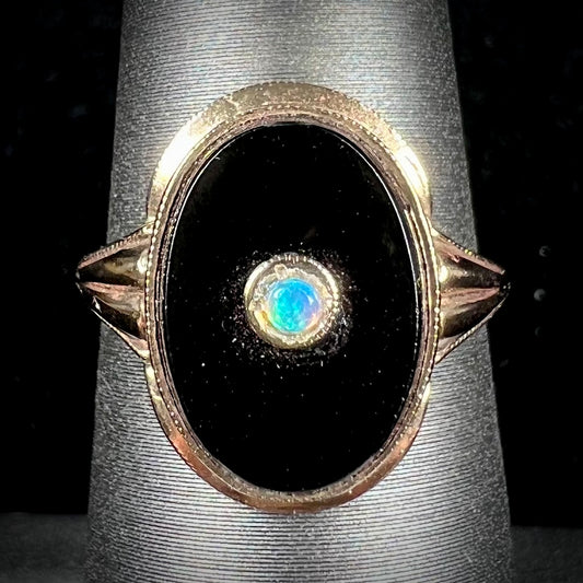 A yellow gold onyx ring set with a round cabochon cut opal bezel set into the onyx.