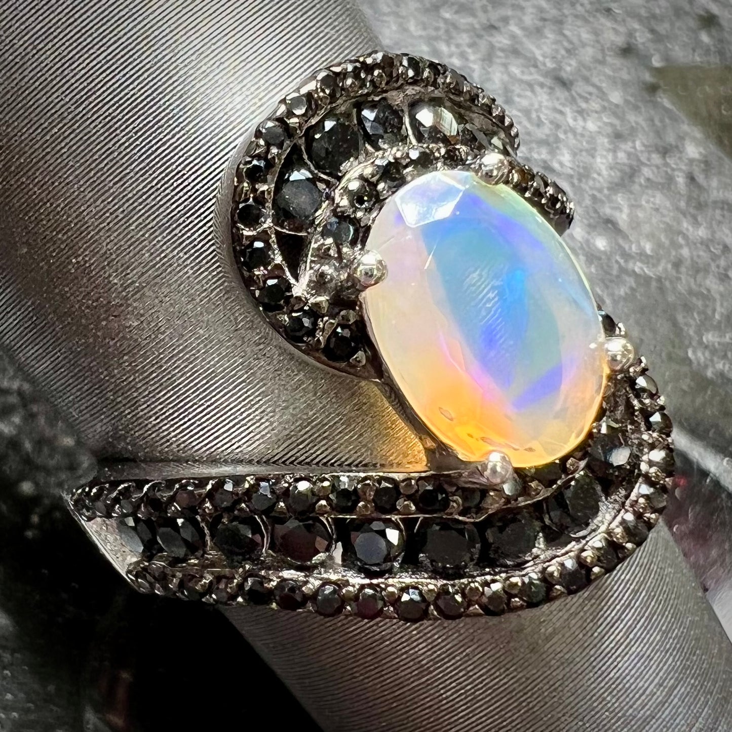 A sterling silver ring set with round black spinel stones and an oval cut, faceted Ethiopian opal.
