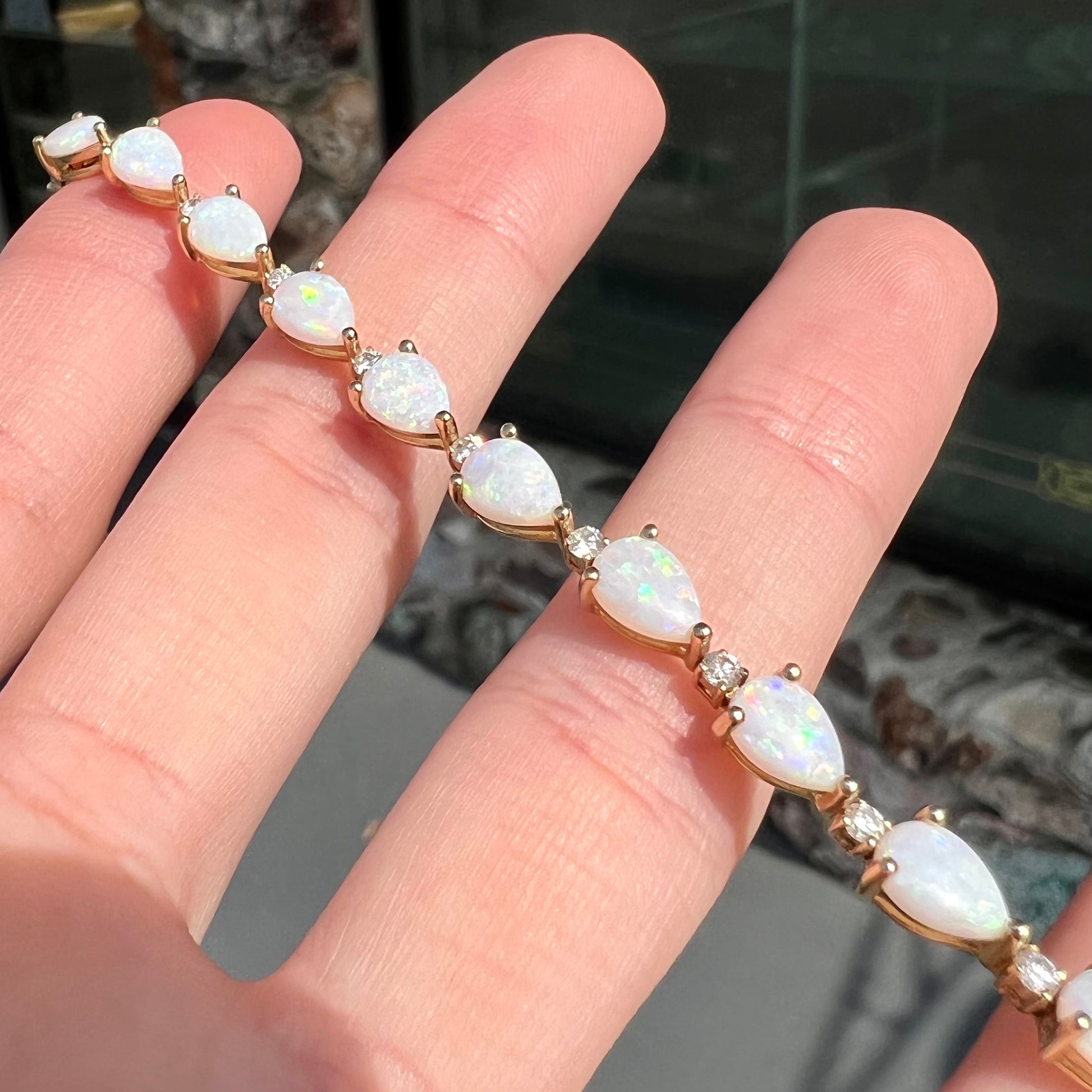 A ladies' gold tennis style bracelet set with pear shaped white crystal opals and diamonds.