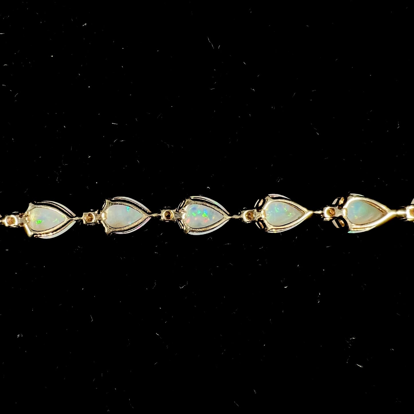 A ladies' gold tennis style bracelet set with pear shaped white crystal opals and diamonds.