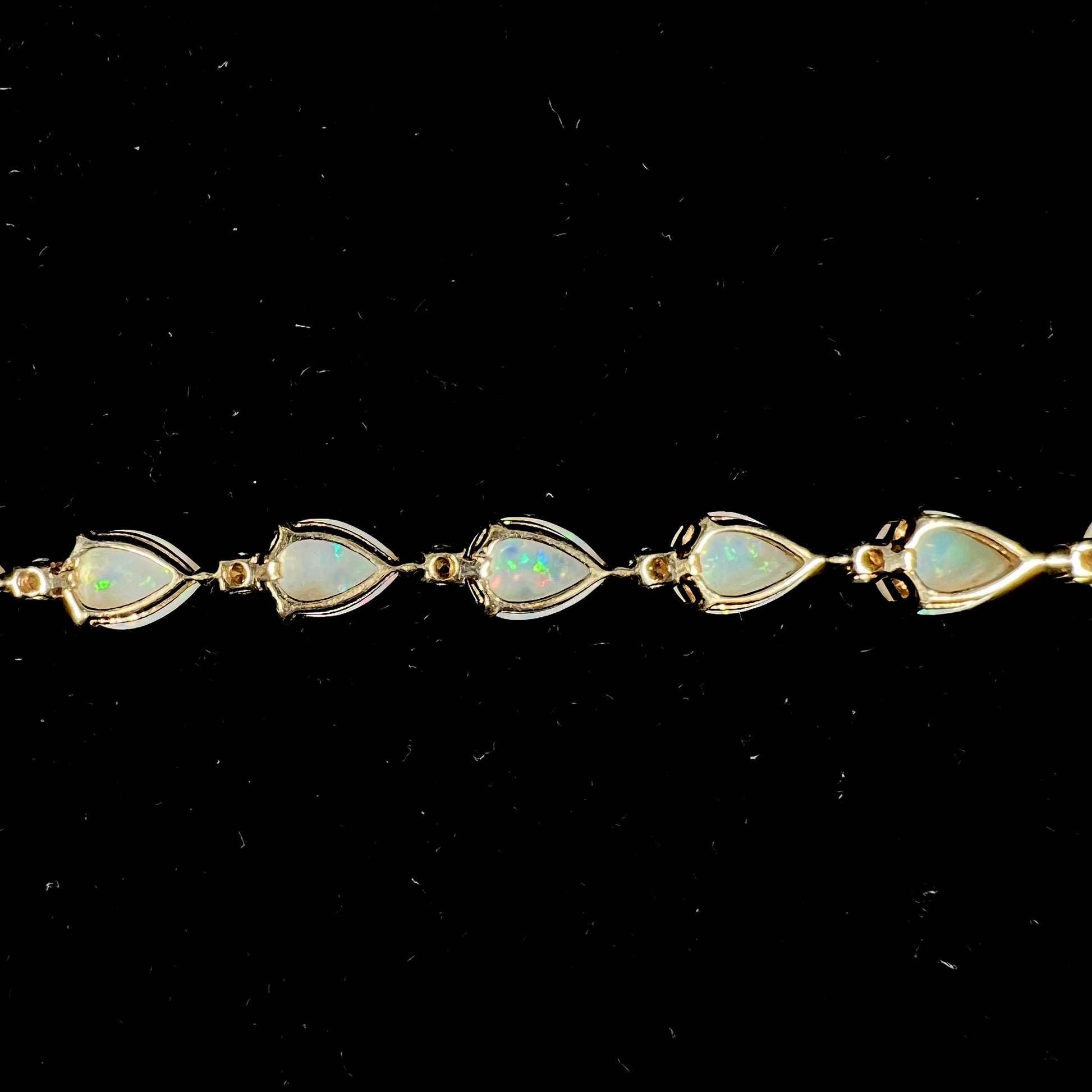 A ladies' gold tennis style bracelet set with pear shaped white crystal opals and diamonds.