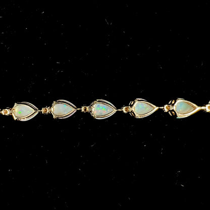 A ladies' gold tennis style bracelet set with pear shaped white crystal opals and diamonds.