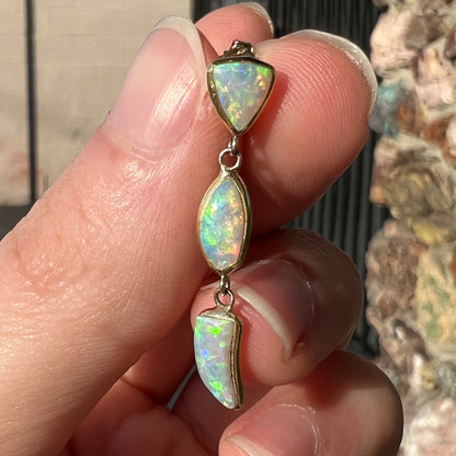 A pair of yellow gold push-back dangle earrings set with three white crystal opals in each.