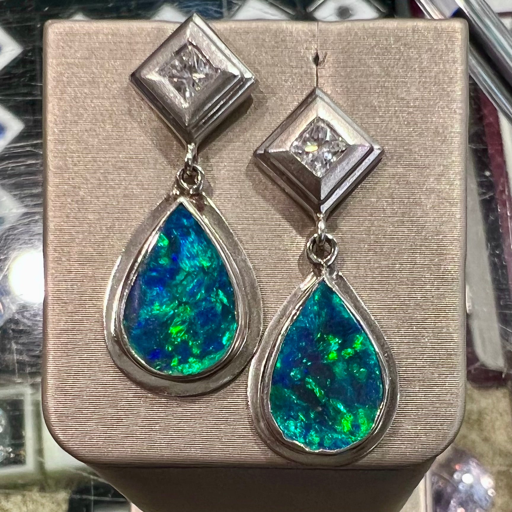 Black crystal opal dangle earrings with blue body color and green play of color set with princess cut diamonds in platinum.