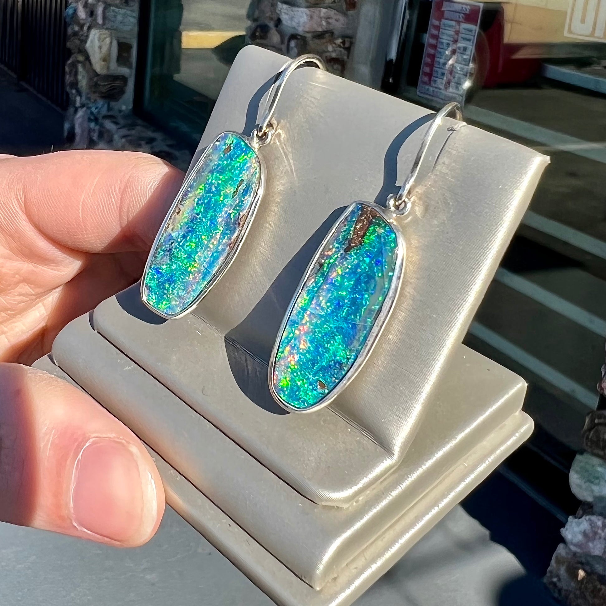 A pair of white gold boulder opal French wire dangle earrings.  The opal is predominantly glimmery blue.