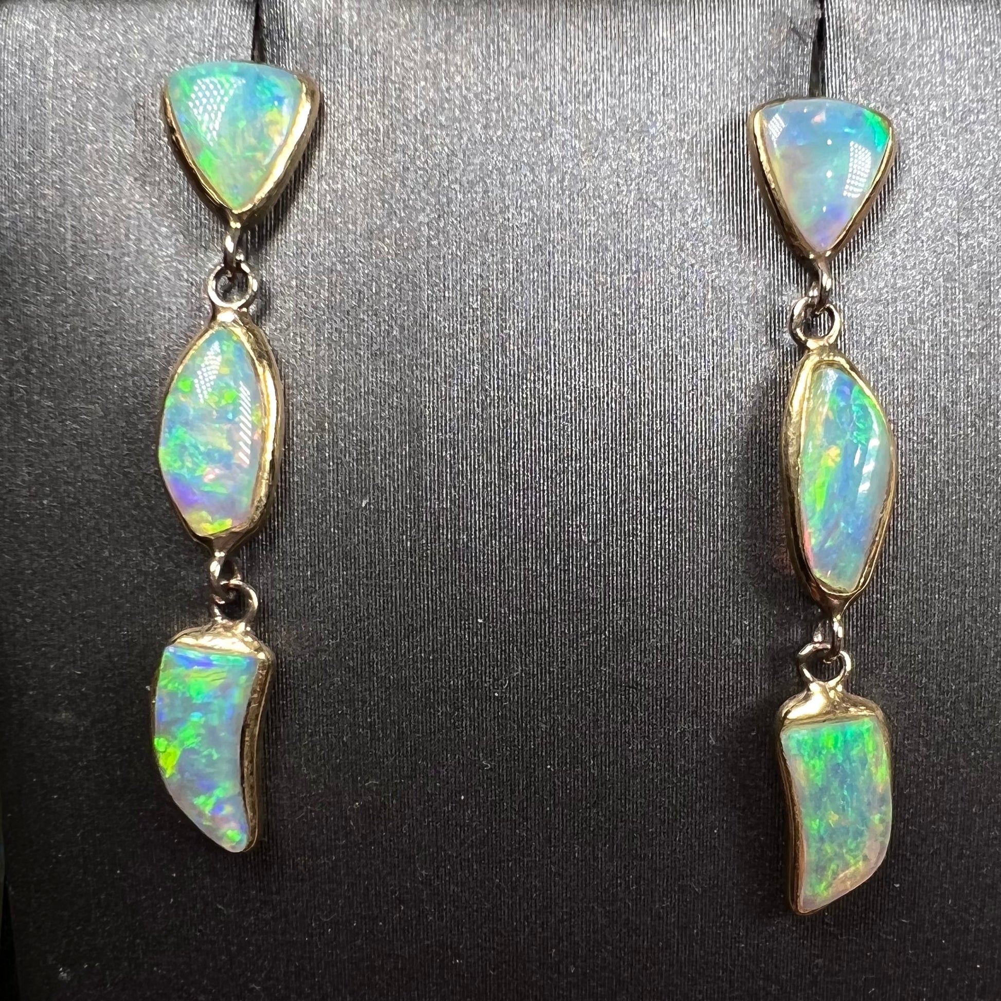 A pair of yellow gold push-back dangle earrings set with three white crystal opals in each.