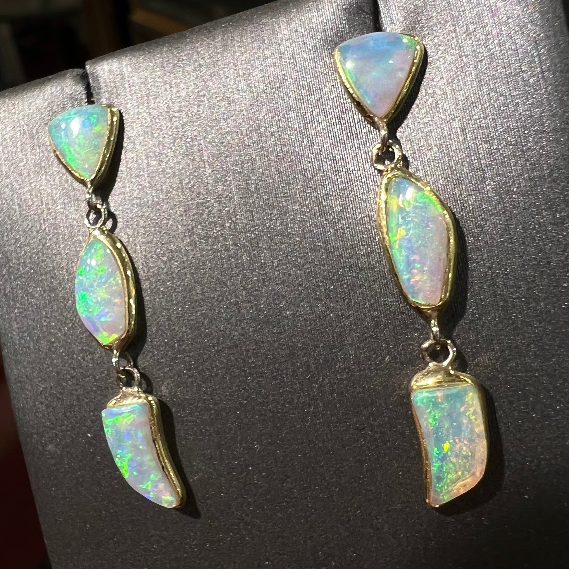 A pair of yellow gold push-back dangle earrings set with three white crystal opals in each.