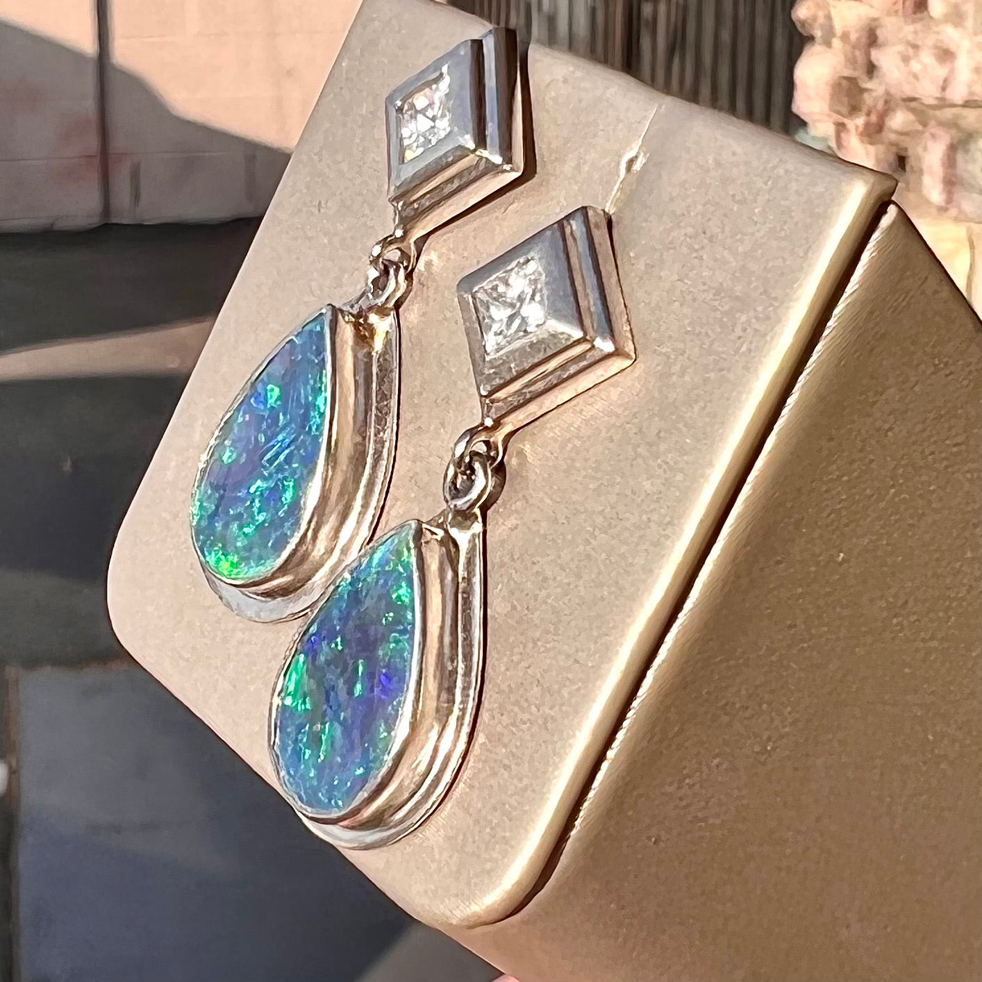 Black crystal opal dangle earrings with blue body color and green play of color set with princess cut diamonds in platinum.