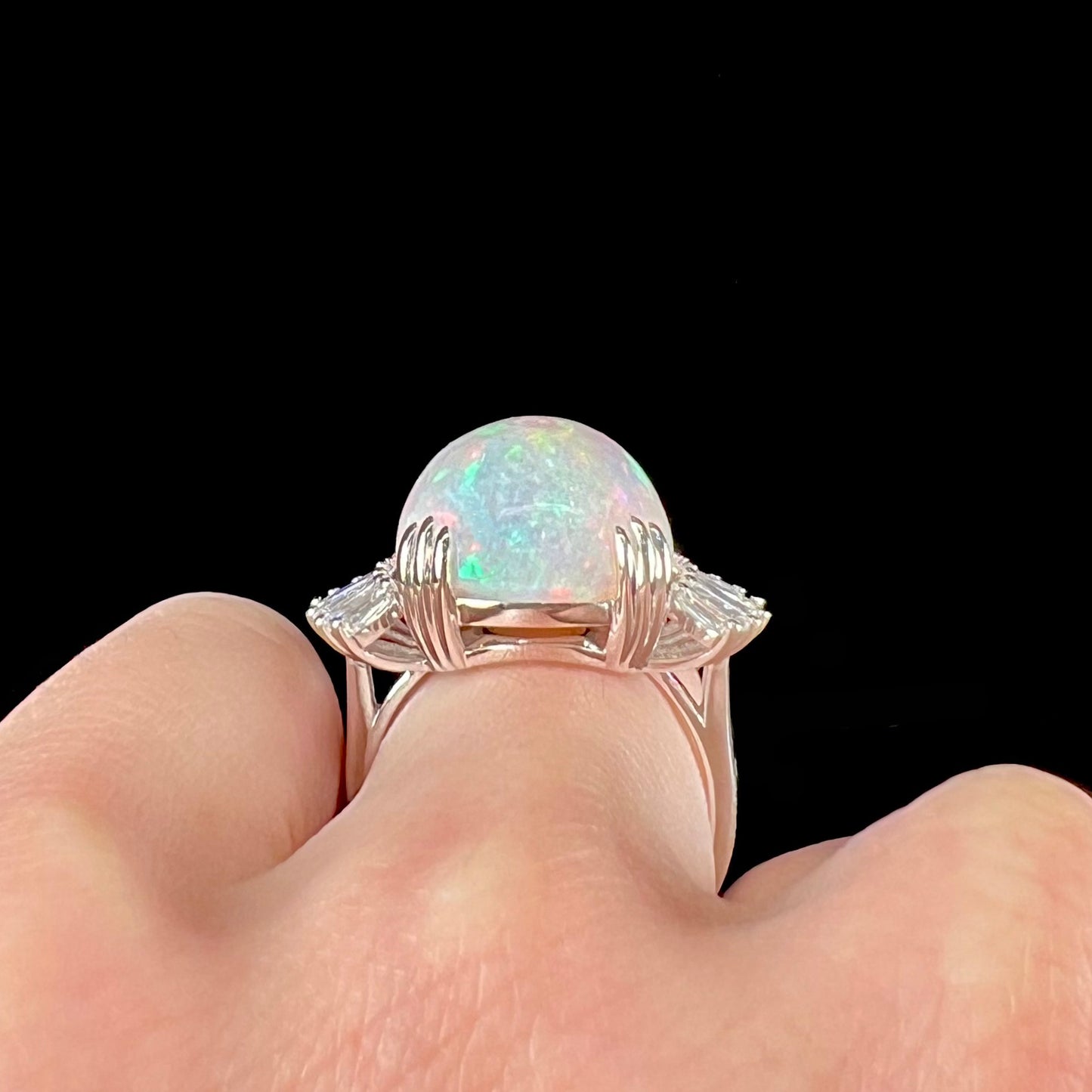 An oval cabochon cut opal mounted in a ladies' white gold ring between tapered baguette cut diamonds.