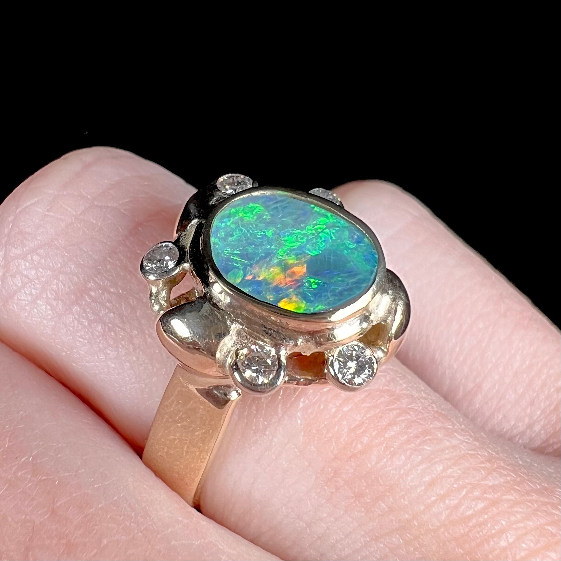 A ladies' yellow gold oval cut natural black opal ring set with five round accent diamonds.