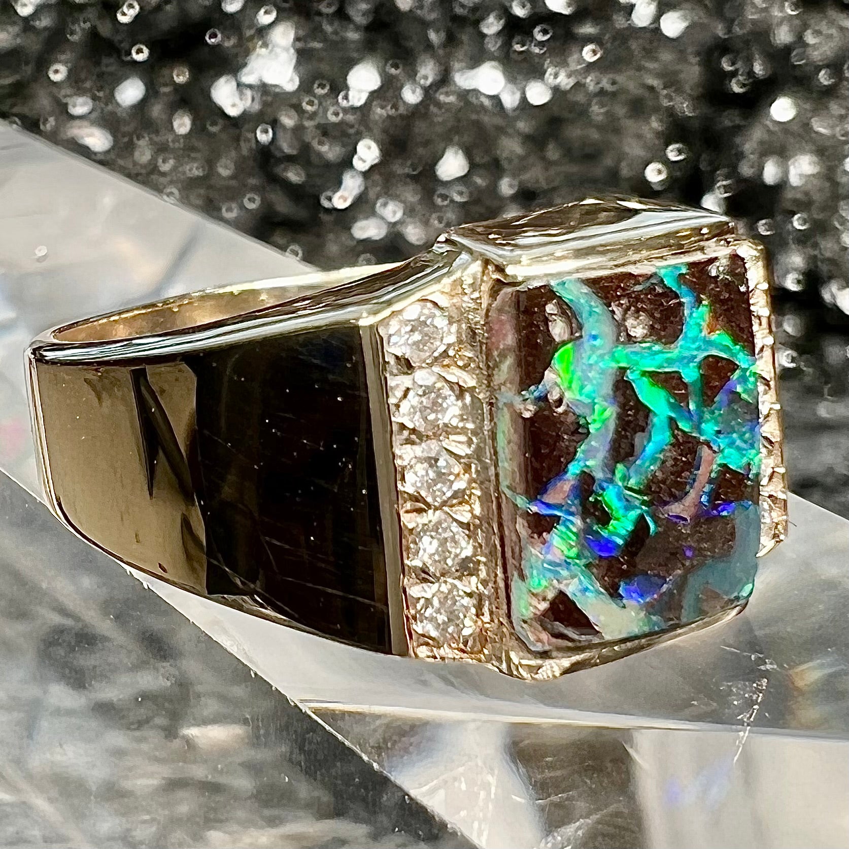 A men's gold boulder opal and diamond ring.  The opal shows blue and green colors.