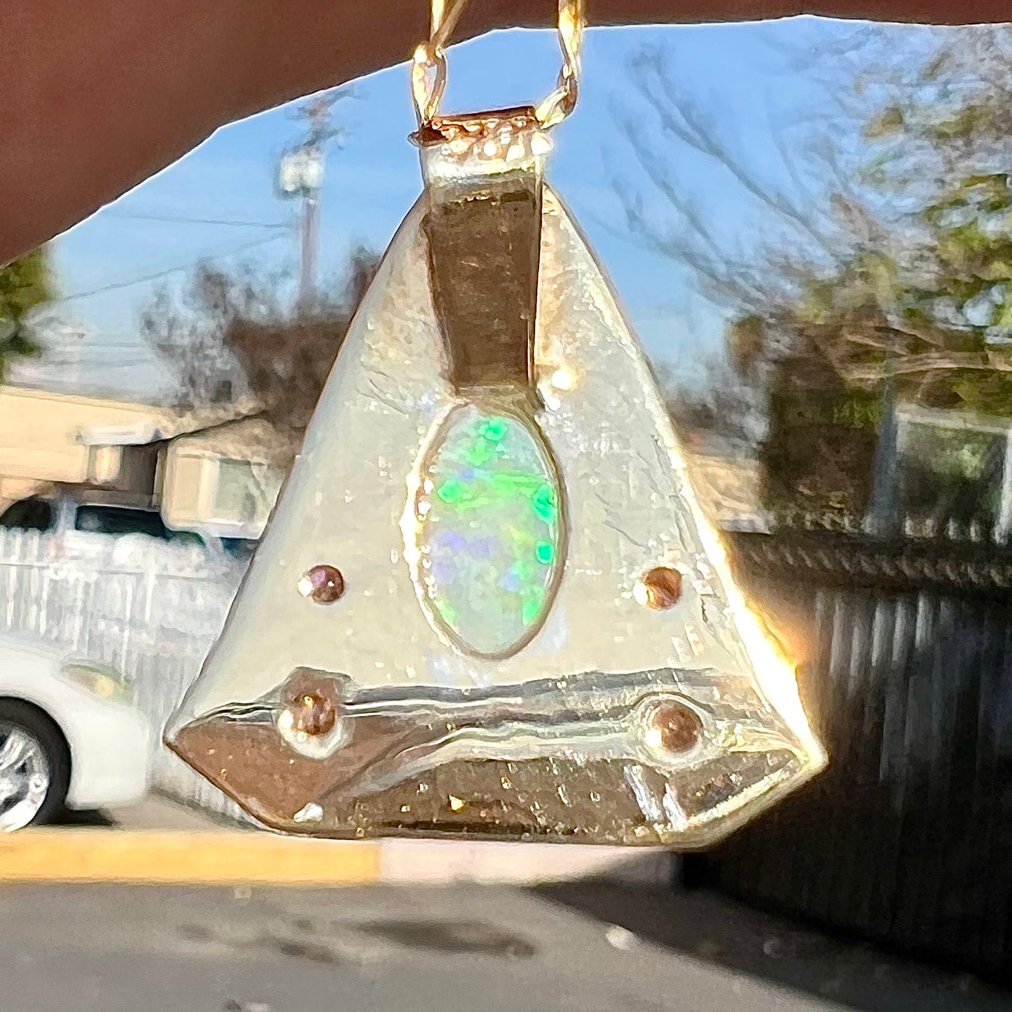 A triangular gold pendant set with five round diamonds and a white crystal opal with green fire.