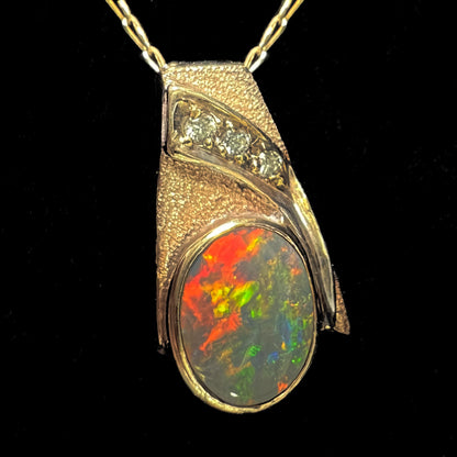 A yellow gold natural, Australian black opal necklace set with three round diamond accents.