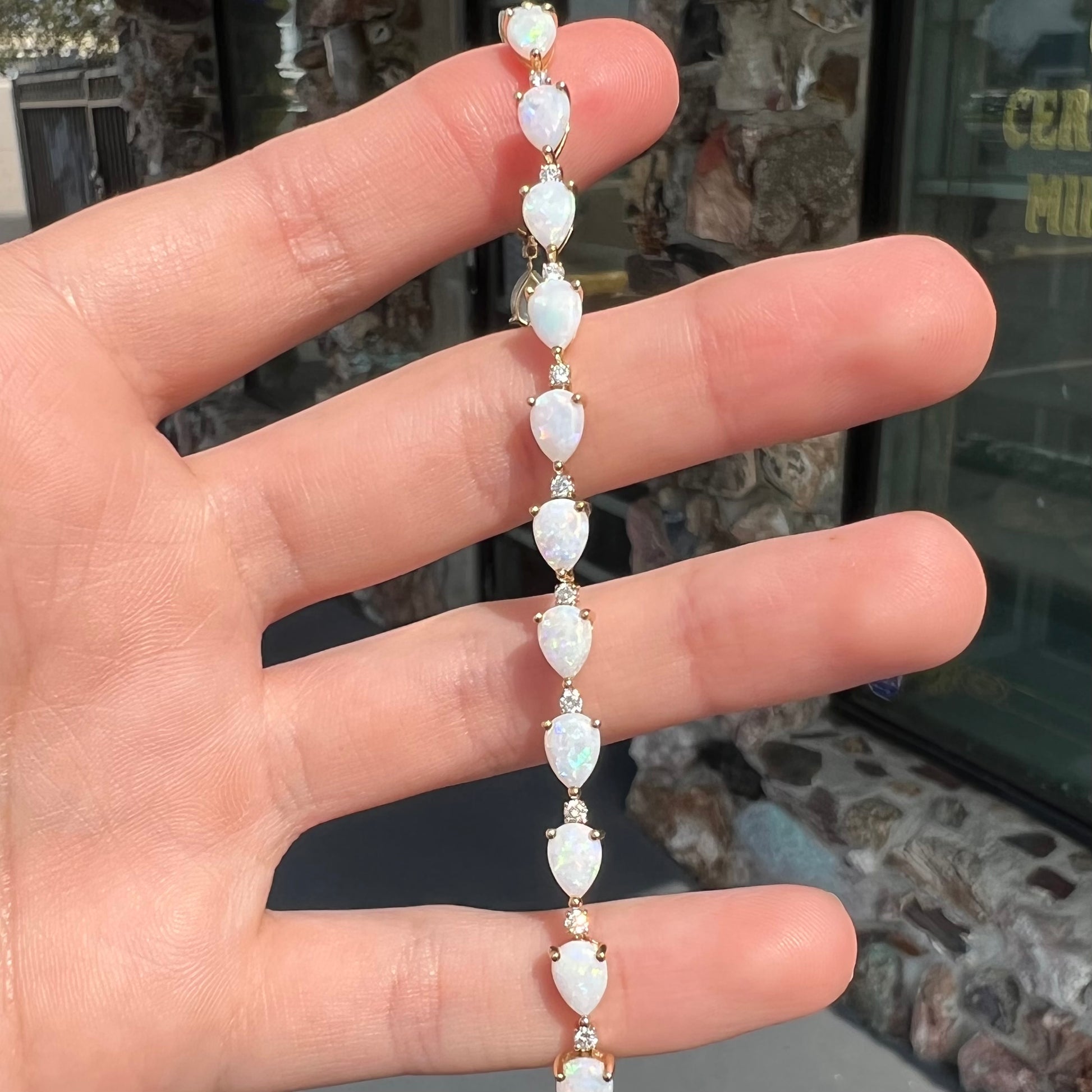 A ladies' gold tennis style bracelet set with pear shaped white crystal opals and diamonds.