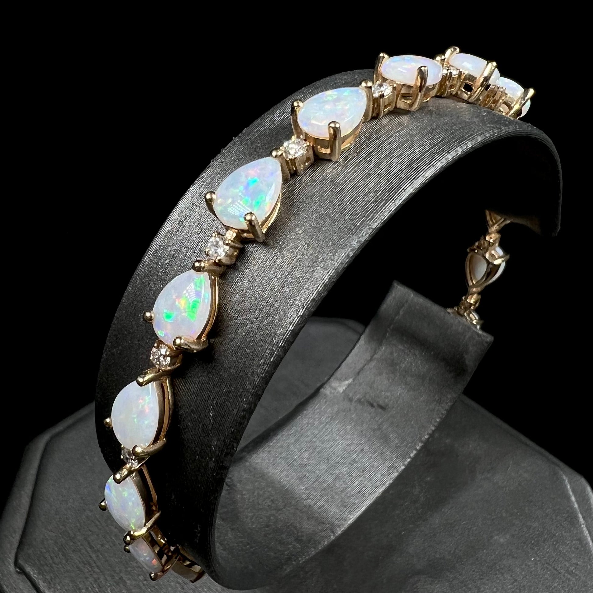 A ladies' gold tennis style bracelet set with pear shaped white crystal opals and diamonds.