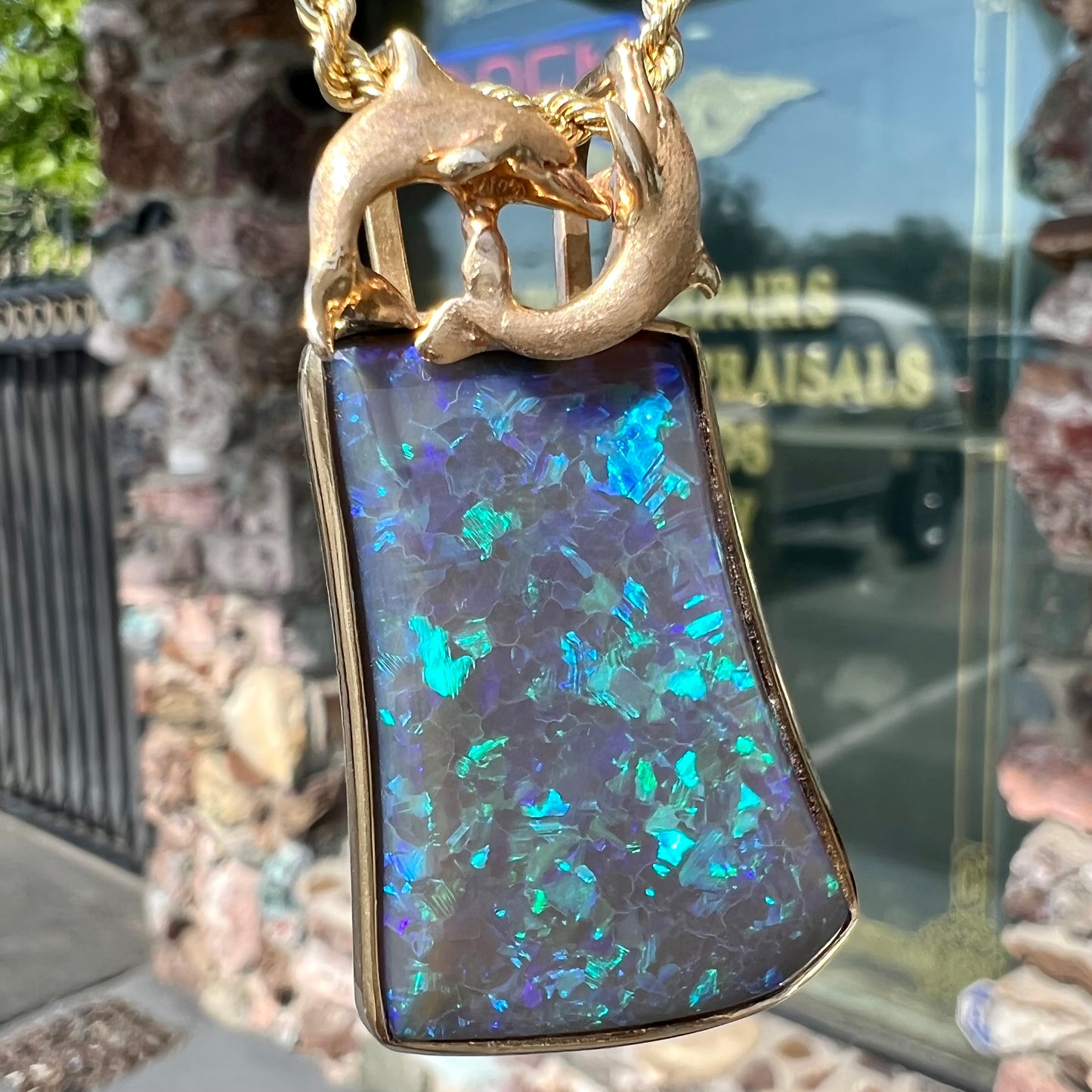 A gold freeform cut black opal bezel pendant cast with two dolphins on top of the opal.