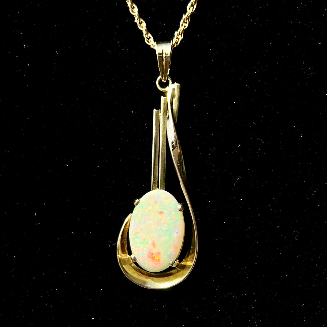 A handmade gold drop pendant set with an oval cabochon cut white crystal opal.