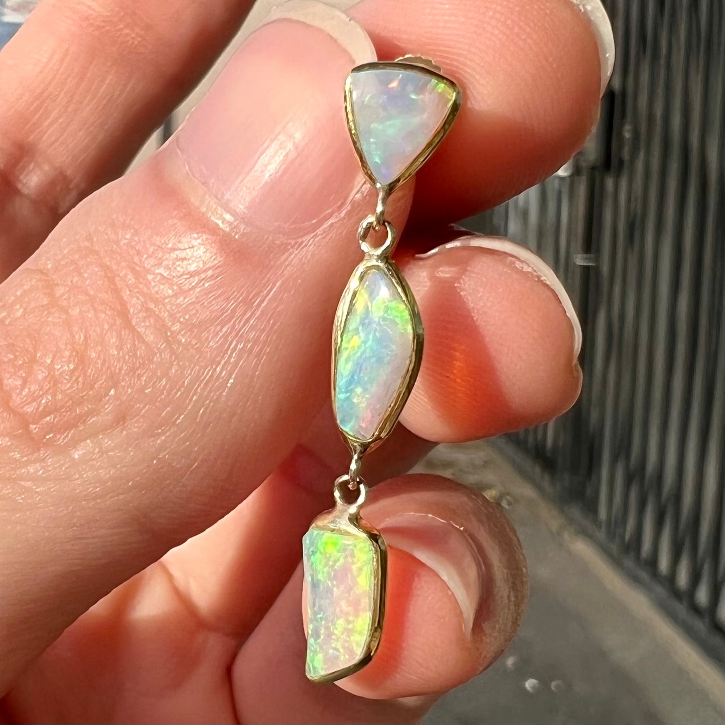 A pair of yellow gold push-back dangle earrings set with three white crystal opals in each.