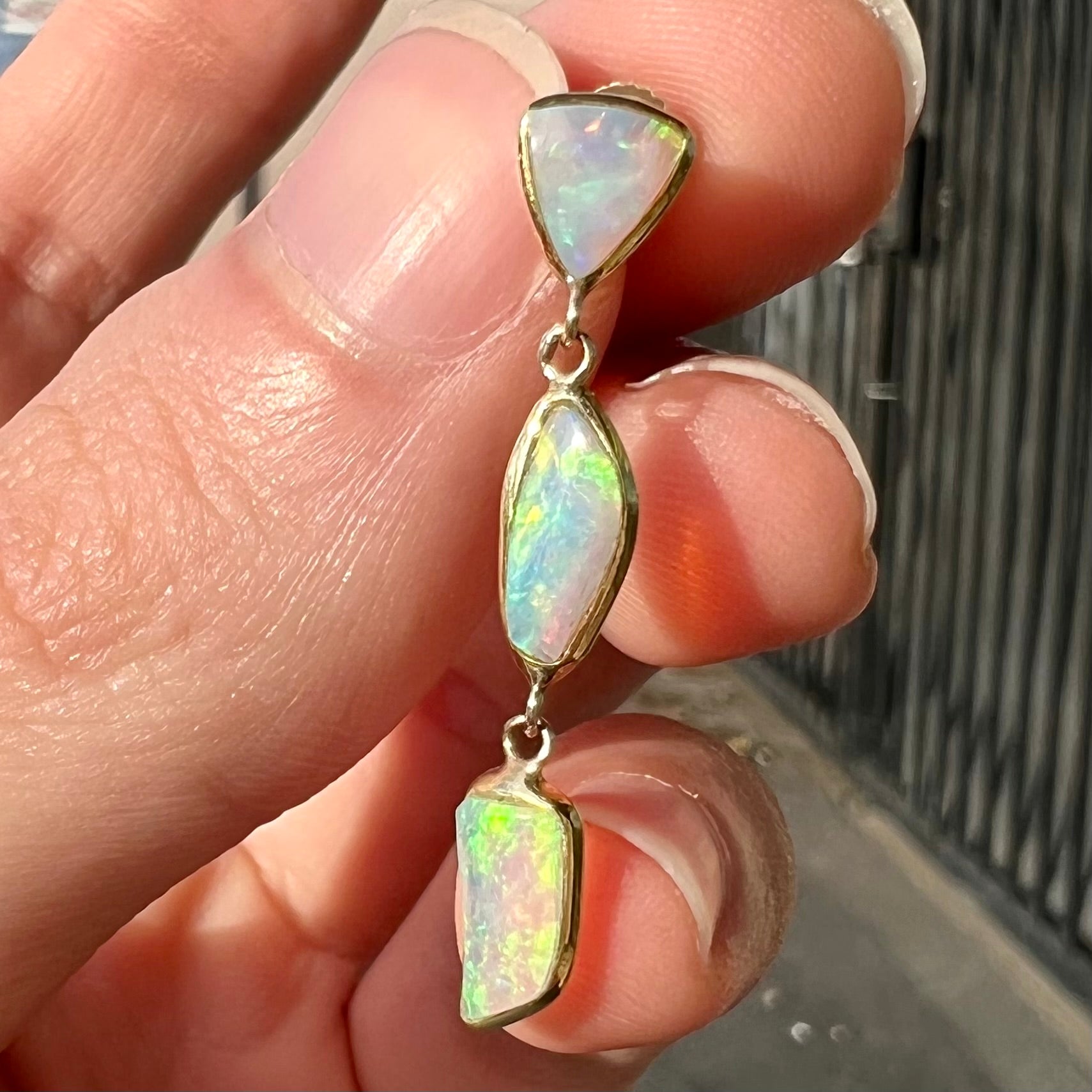 A pair of yellow gold push-back dangle earrings set with three white crystal opals in each.