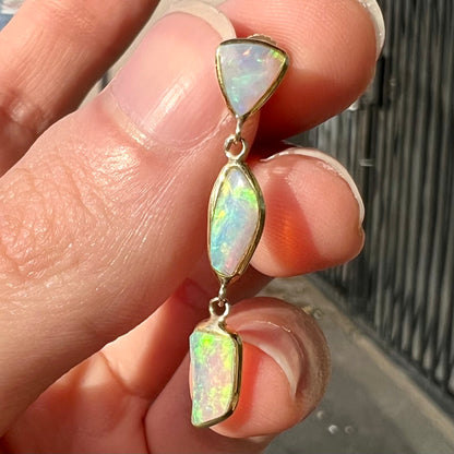 A pair of yellow gold push-back dangle earrings set with three white crystal opals in each.