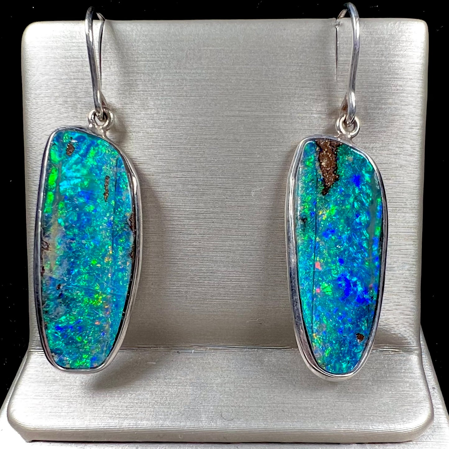 A pair of white gold boulder opal French wire dangle earrings.  The opal is predominantly glimmery blue.