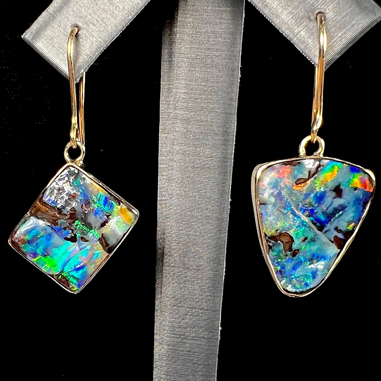 An asymmetric pair of French wire dangle yellow gold boulder opal earrings.  One opal is a square, and the other is a triangle.