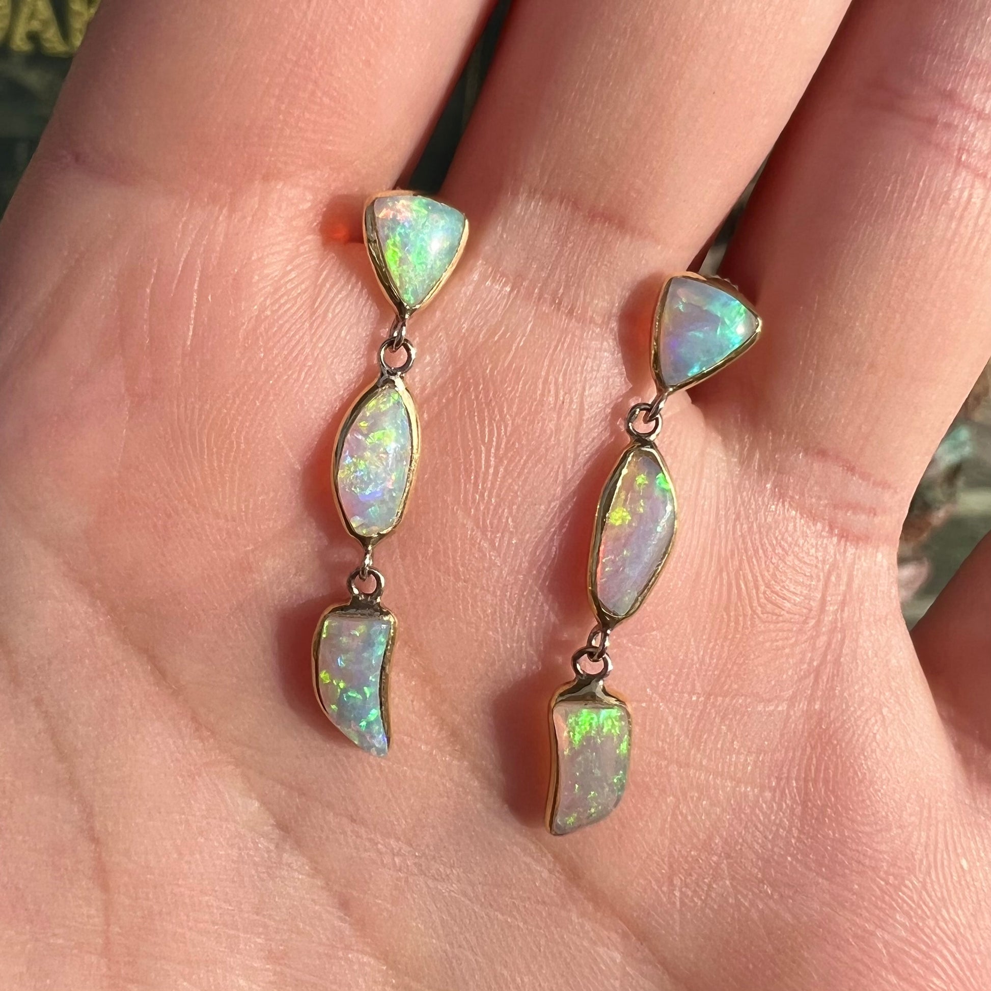 A pair of yellow gold push-back dangle earrings set with three white crystal opals in each.