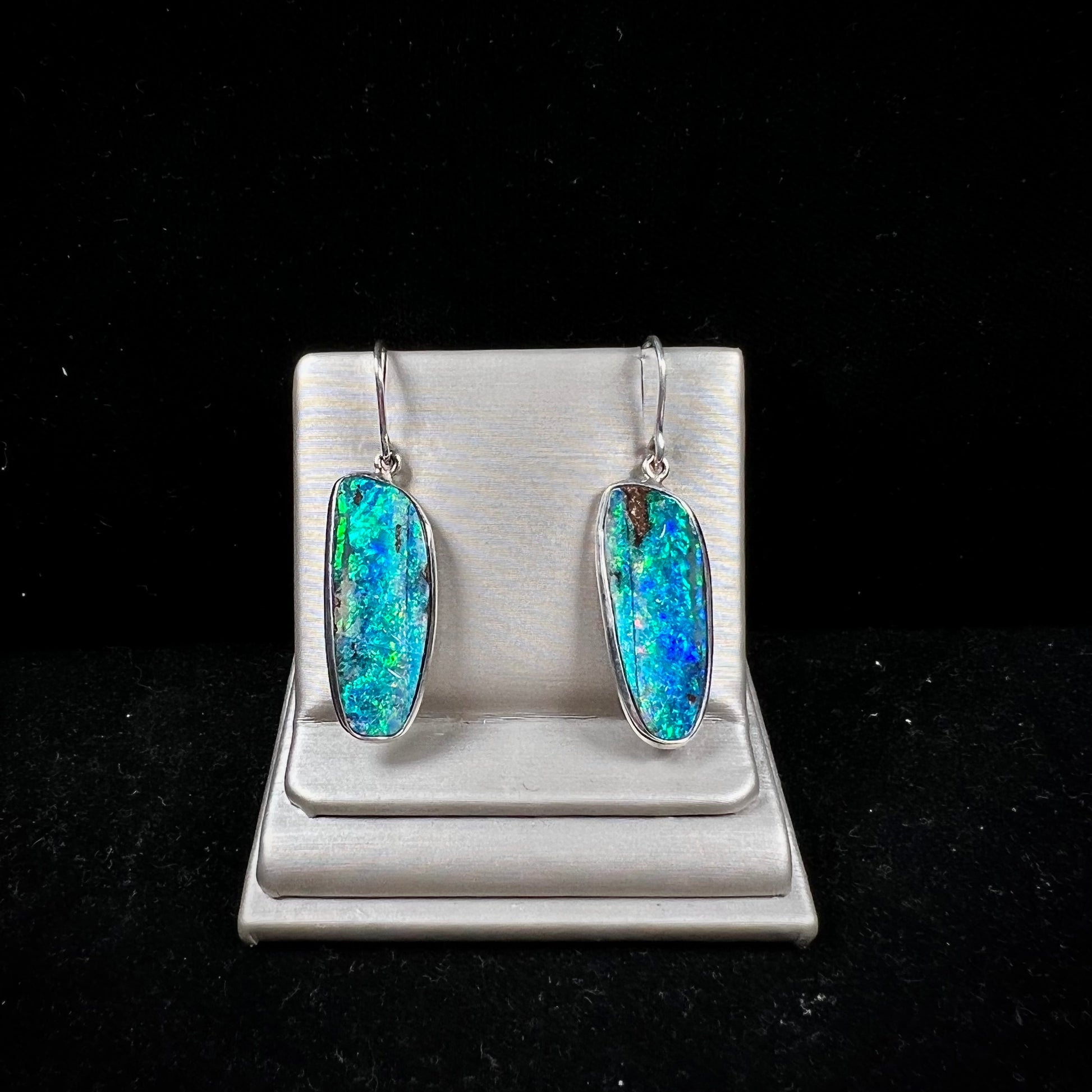 A pair of white gold boulder opal French wire dangle earrings.  The opal is predominantly glimmery blue.