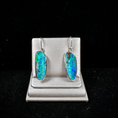 A pair of white gold boulder opal French wire dangle earrings.  The opal is predominantly glimmery blue.