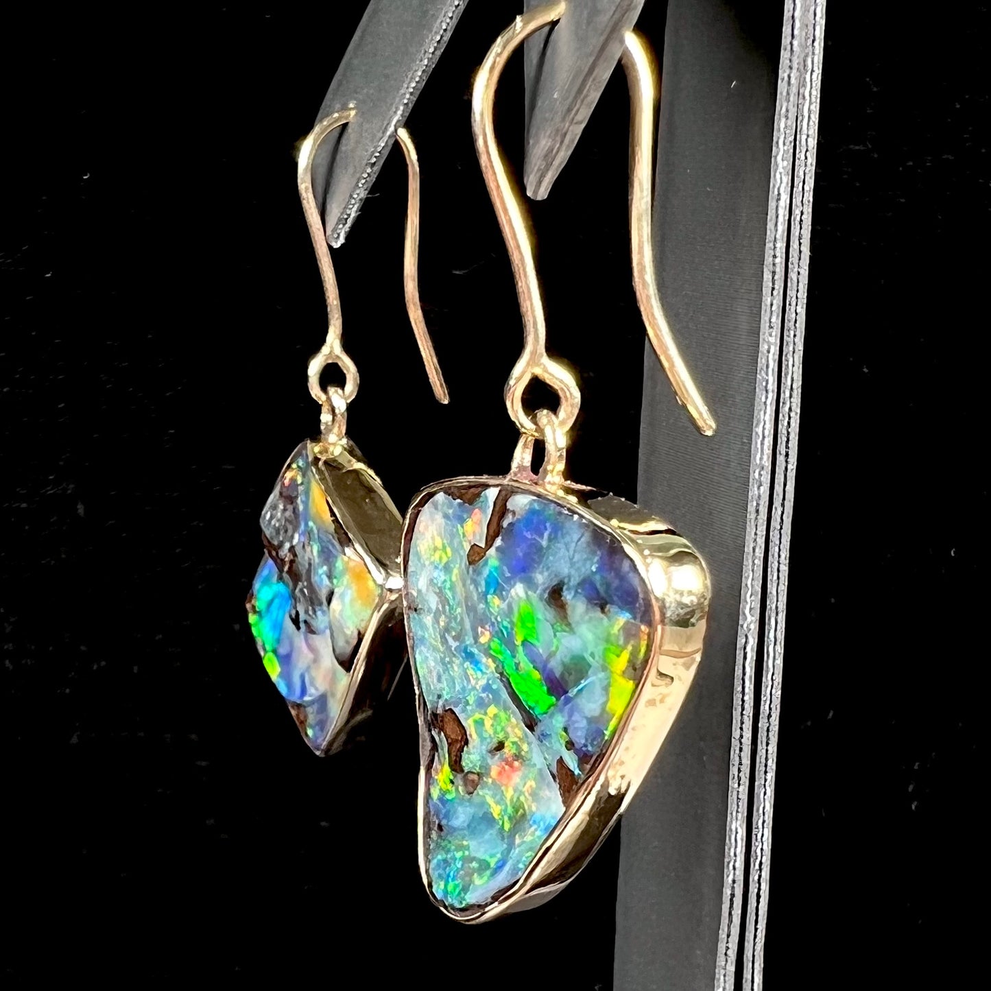 An asymmetric pair of French wire dangle yellow gold boulder opal earrings.  One opal is a square, and the other is a triangle.