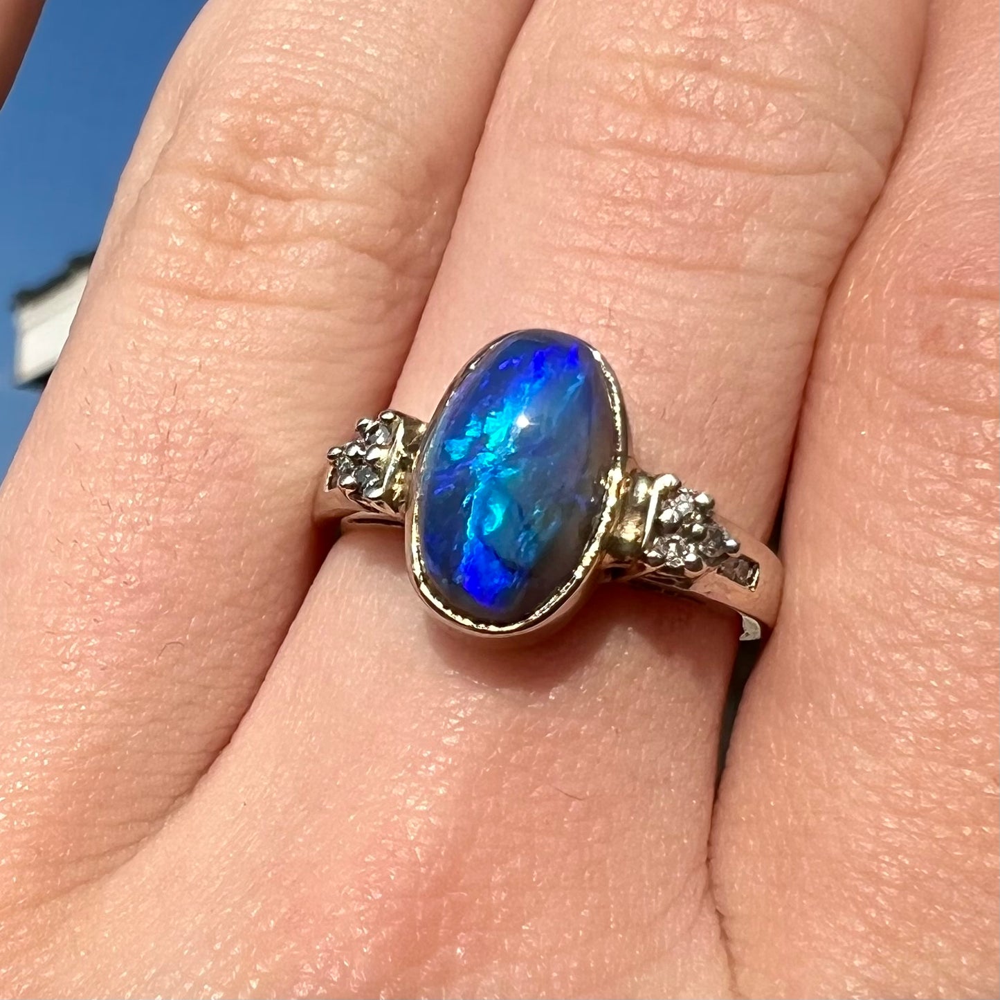 A white gold ring set with a Lightning Ridge black opal and diamond accents.  The opal displays a cat's eye pattern.