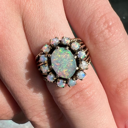 Vintage yellow gold oval opal cabochon ring set with 12 round opals in a halo around the center stone.