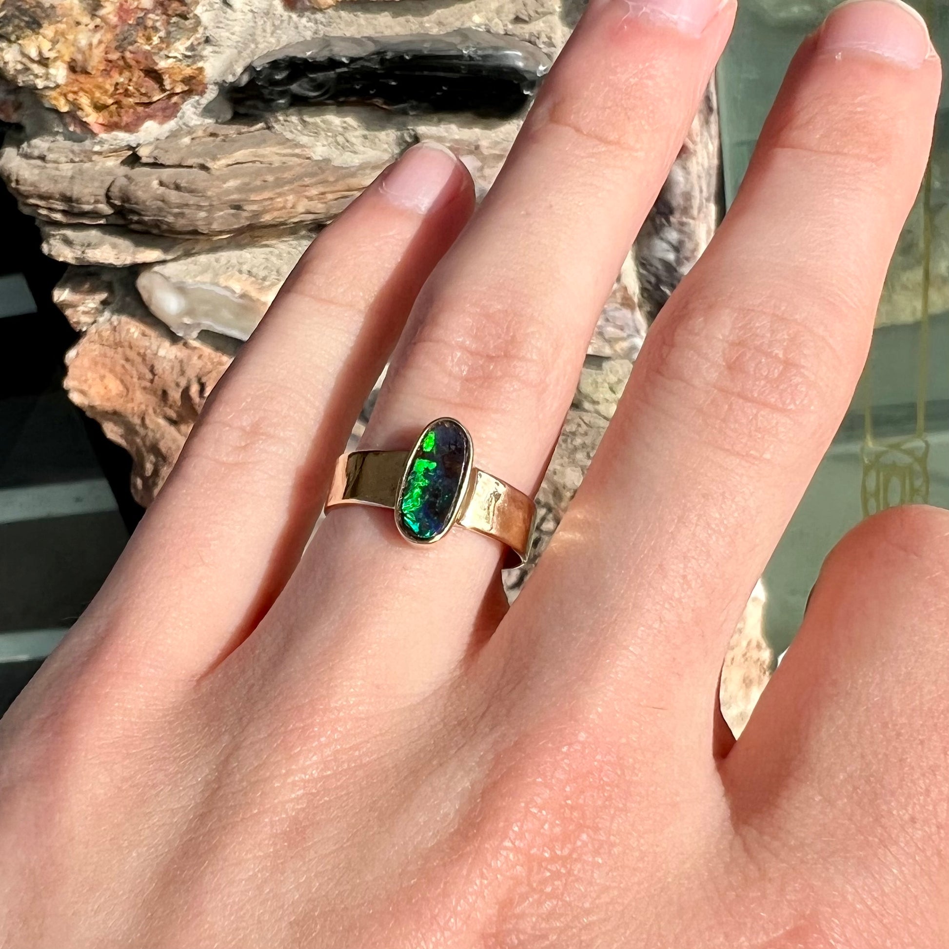 A blue green oval cabochon cut Australian boulder opal set in a yellow gold solitaire ring.