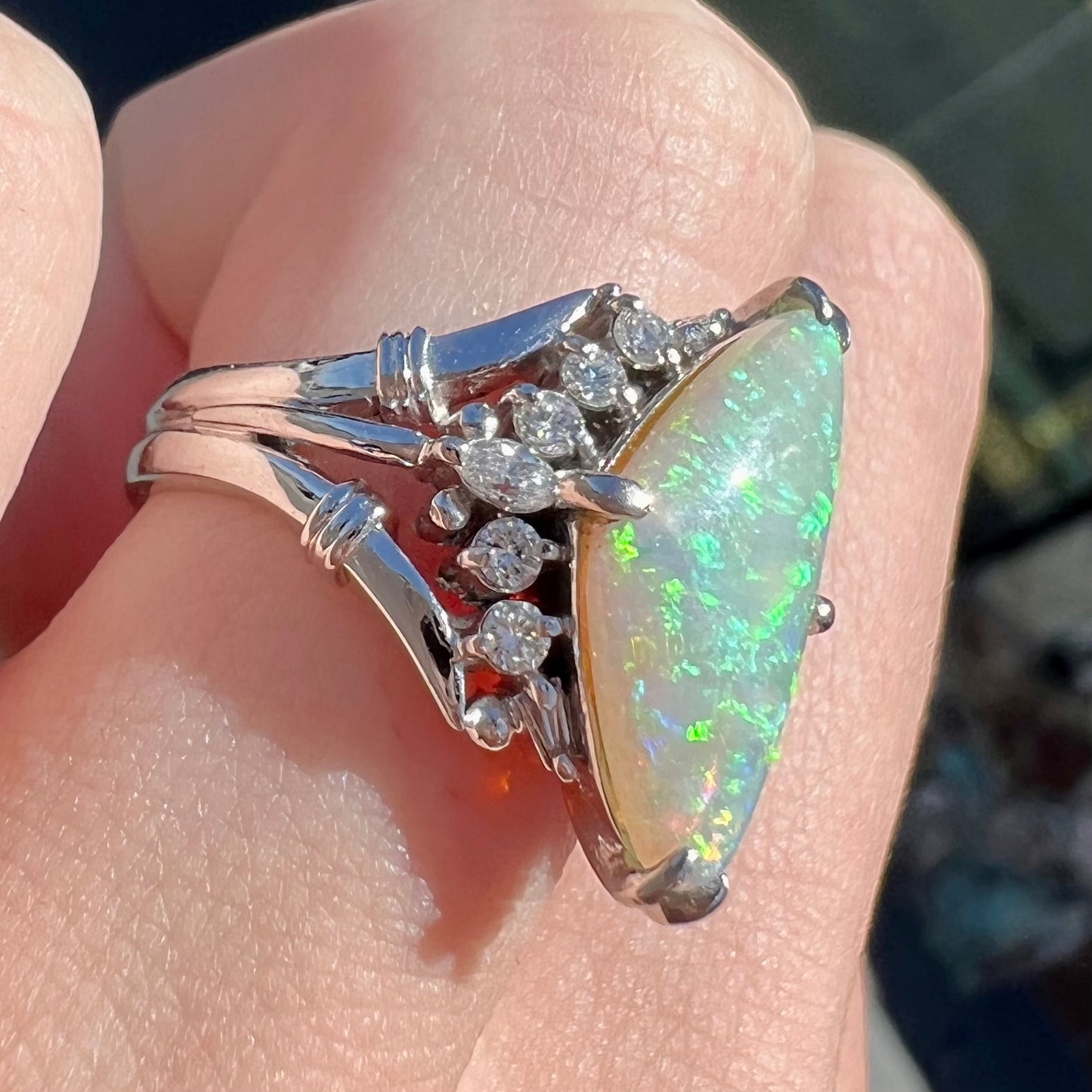 A freeform triangular cabochon cut Lightning Ridge white crystal opal set with diamonds in an ornate platinum split shank setting.