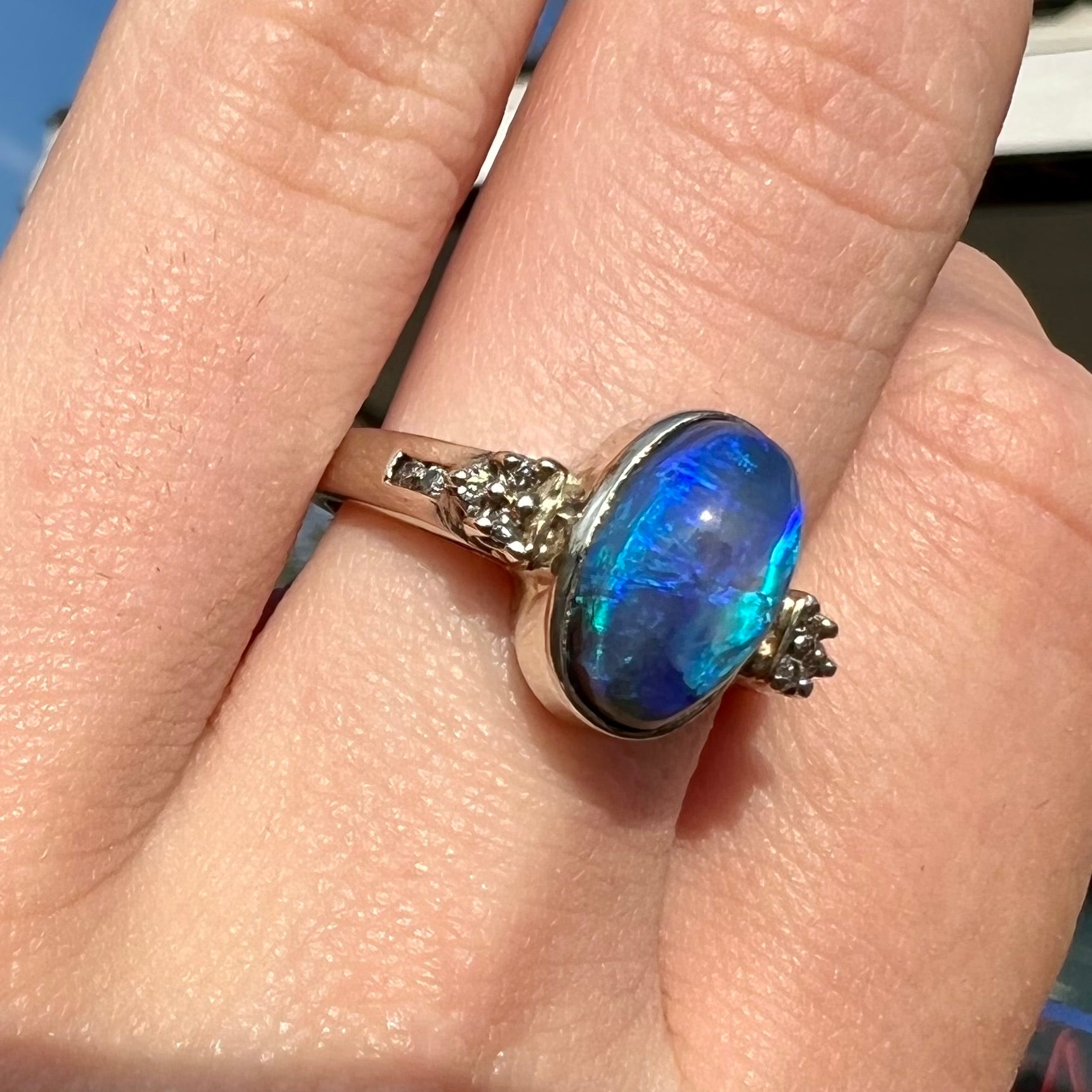 A white gold ring set with a Lightning Ridge black opal and diamond accents.  The opal displays a cat's eye pattern.